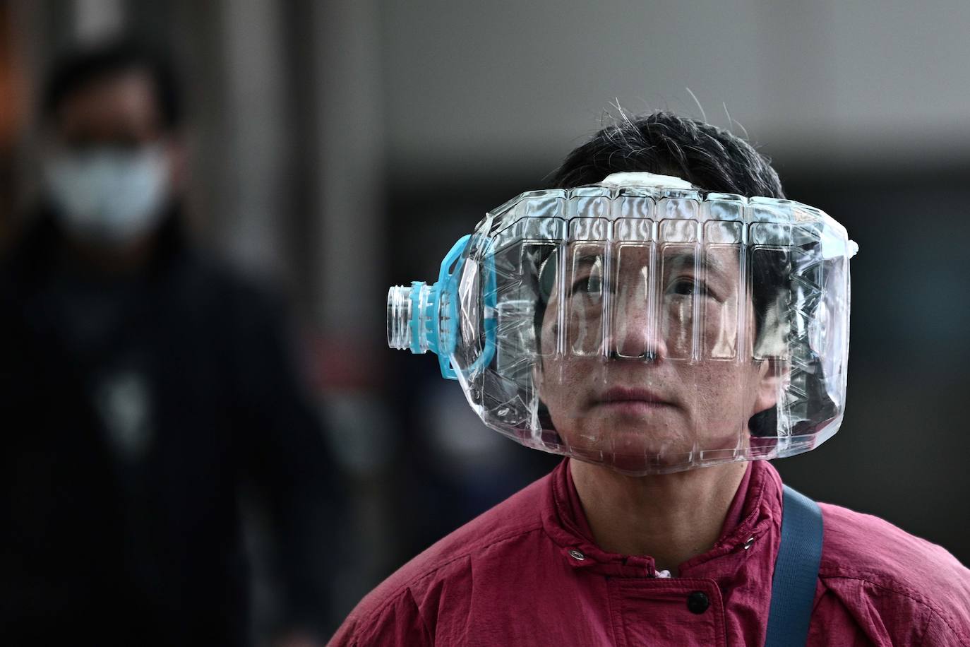 Una persona usa una botella de agua de plástico para cubrirse la cara, mientras camina sobre una pasarela en Hong Kong 