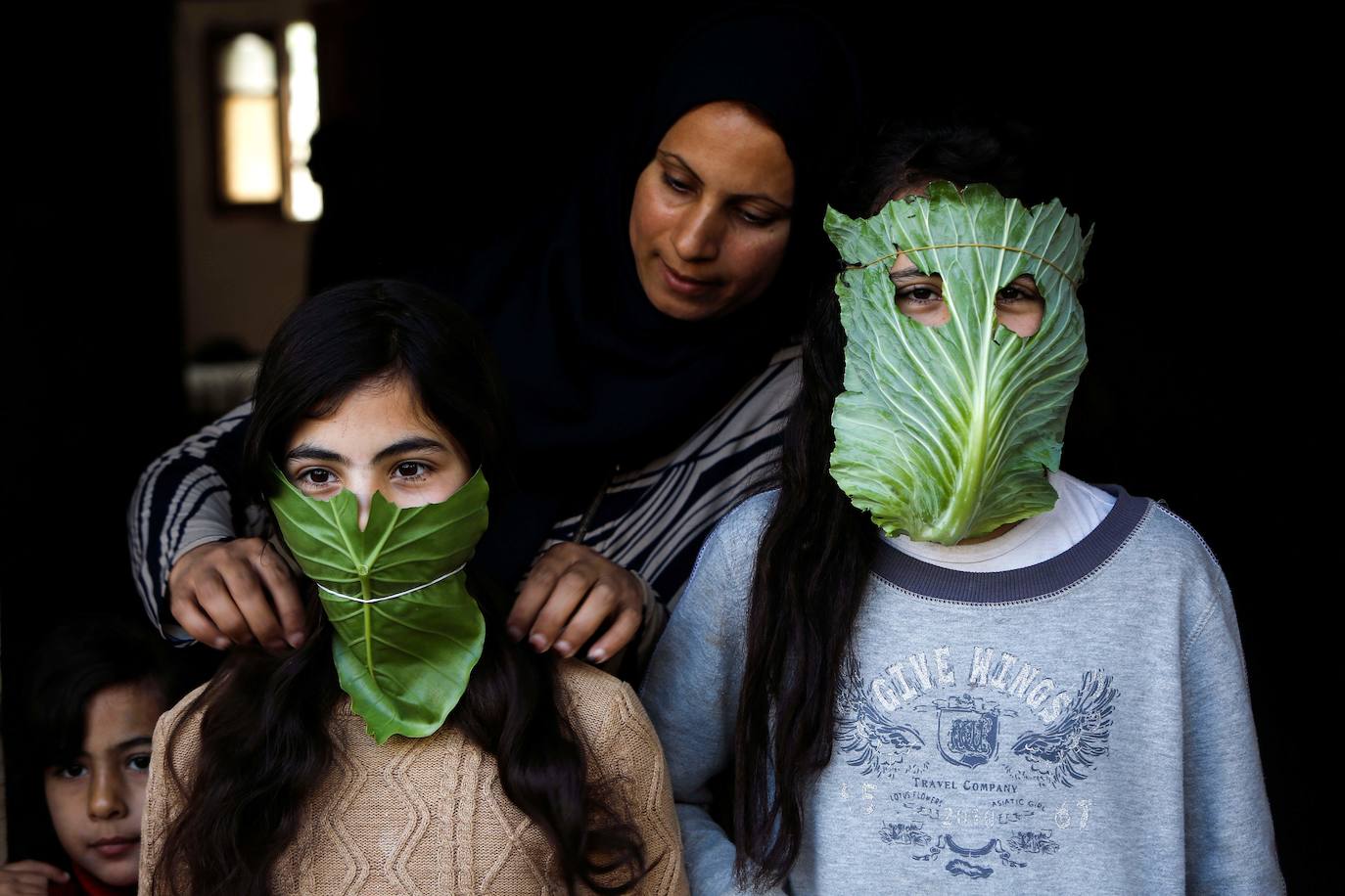 Una madre palestina entretiene a sus hijos con máscaras improvisadas hechas de repollo mientras cocina en Beit Lahia, en el norte de la Franja de Gaza. 