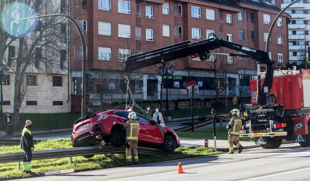 Los bomberos fijan el coche para bajarlo del quitamiedos. 