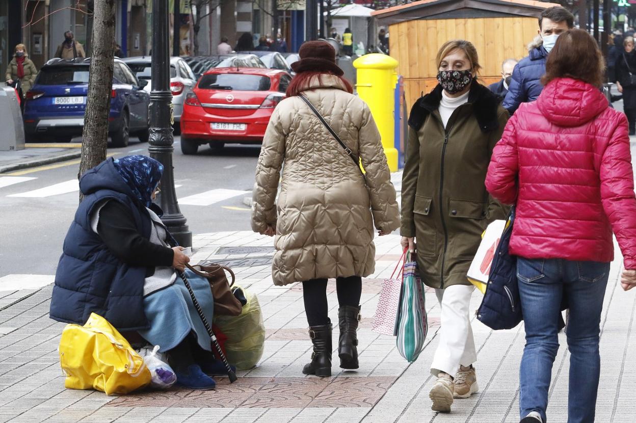Una mujer sin recursos descansa sentada sobre unas bolsas en una calle de Gijón. 