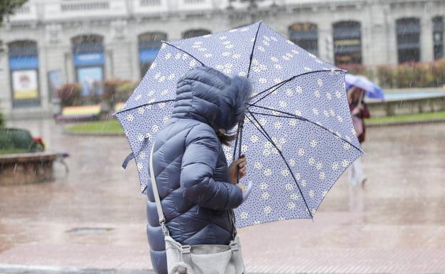 Una mujer se protege de la lluvia y el viento en una calle de Oviedo en una imagen de archivo. 