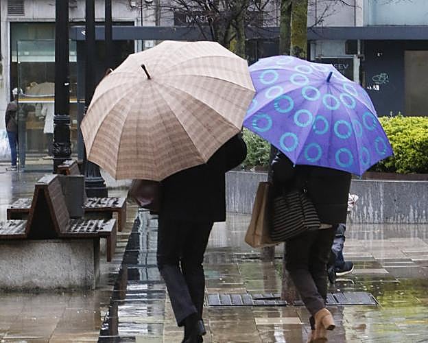 Paseantes en Gijón con las calles mojadas. 