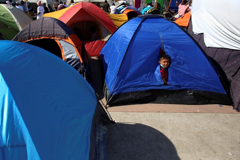 Un niño mira desde una carpa junto a otros migrantes de Centroamérica que acampan fuera del cruce fronterizo de El Chaparral, con la esperanza de cruzar y solicitar asilo en Estados Unidos, en Tijuana, México.