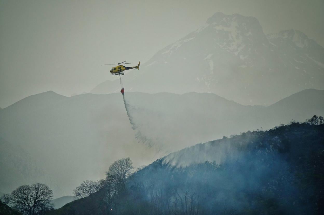 Un helicóptero de Bomberos libera su carga de agua para reducir la temperatura de la zona quemada. En el vídeo: Incendio forestal en El Pedrosu, en Piloña.