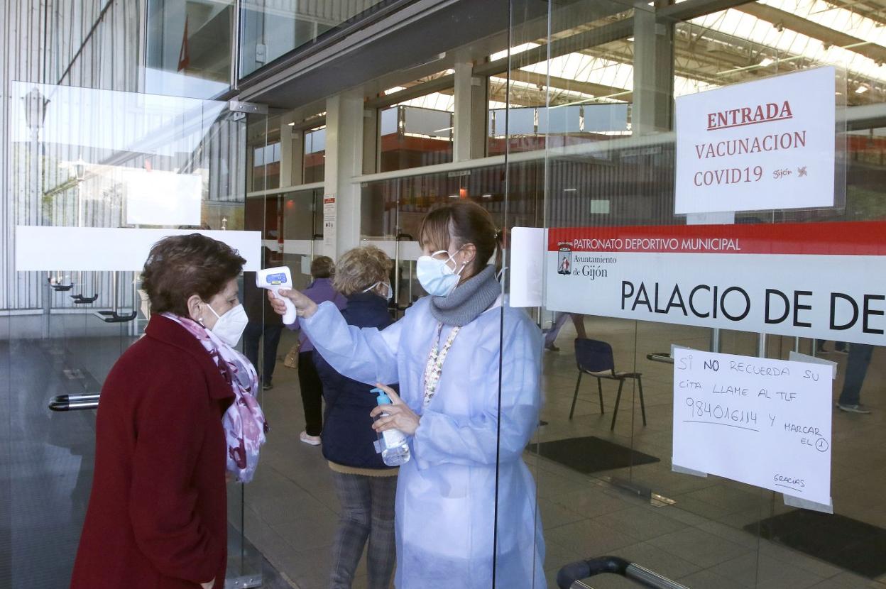 Una sanitaria toma la temperatura a una mujer para entrar al Palacio de Deportes de Gijón para ser vacunada. 