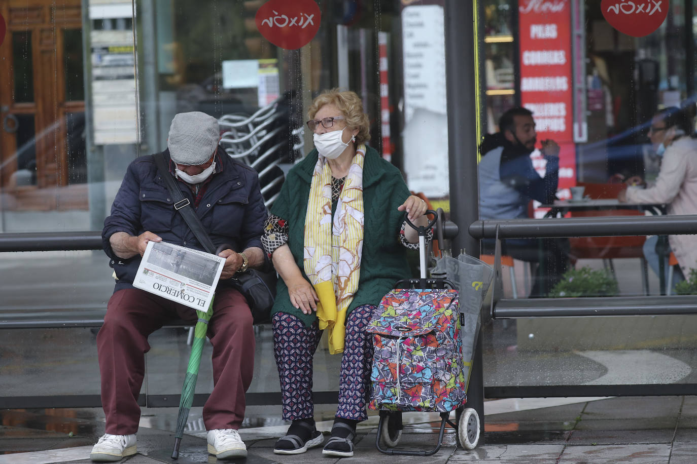 Una pareja espera el autobús en una marquesina, al resguardo del frío.