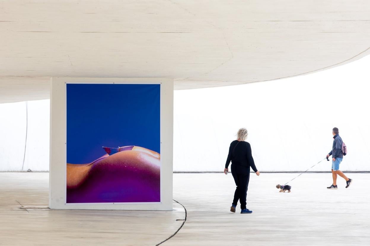 Varios transeúntes pasan junto a la imagen que desató la polémica, expuesta en la plaza del Niemeyer. 