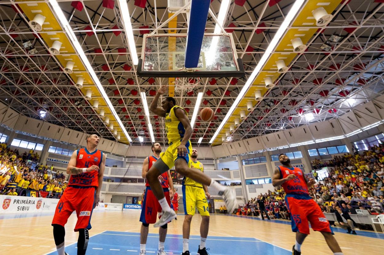 Un jugador del BC CSU Sibiu rumano, de amarillo, machaca la canasta. 