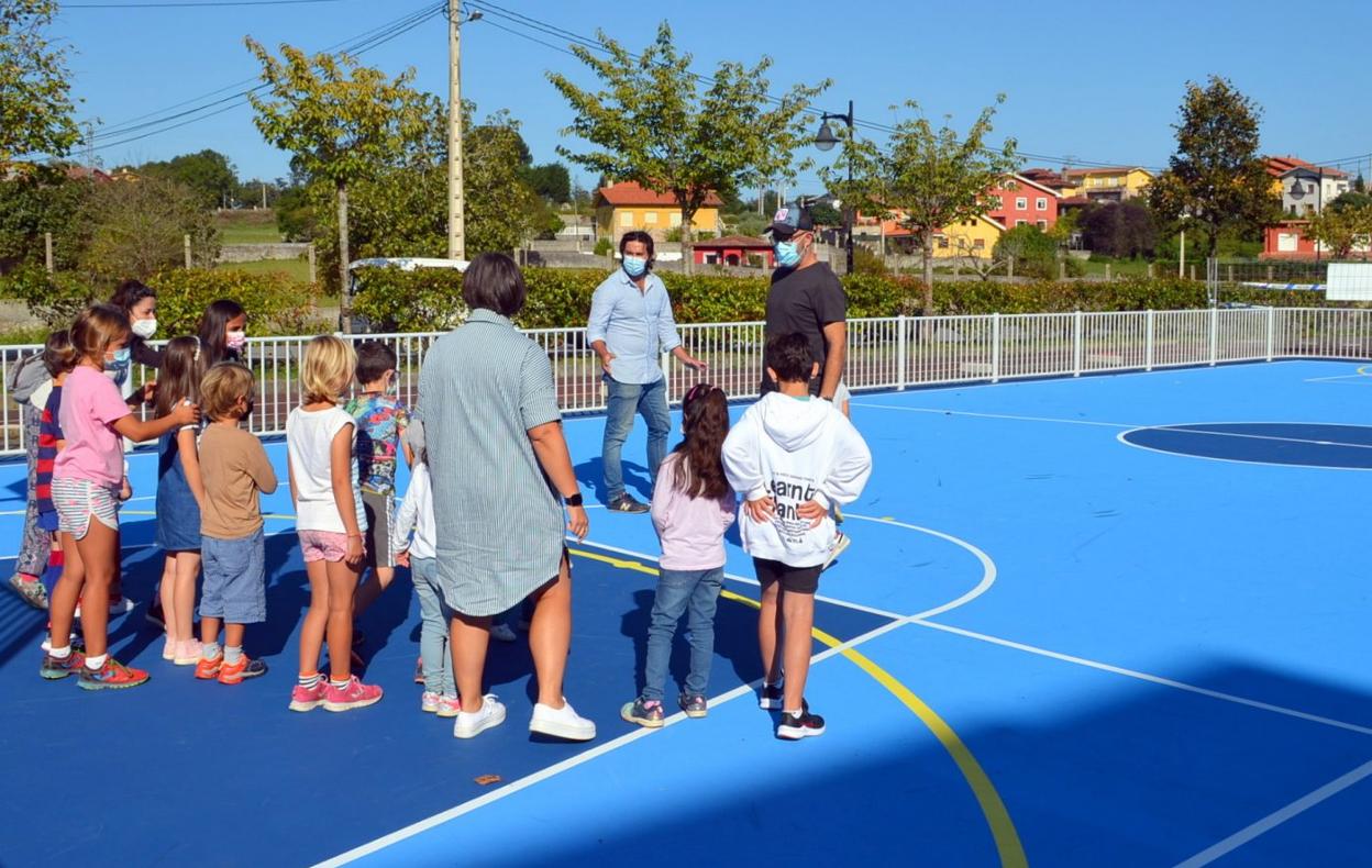 Enrique Riestra e Iván García enseñan la nueva pista polideportiva de Celorio a los niños. 