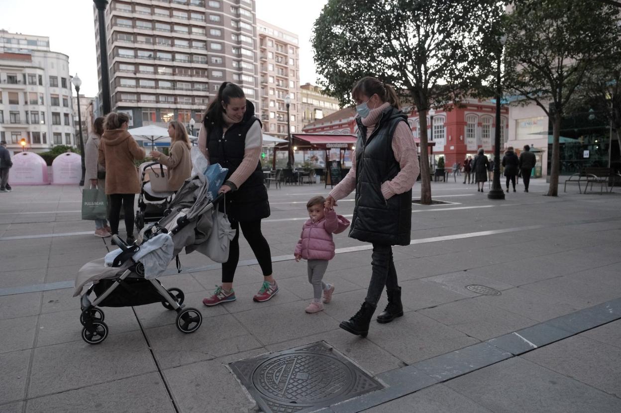 Dos mujeres caminan con una pequeña por la plaza del Seis de Agosto, en Gijón. 