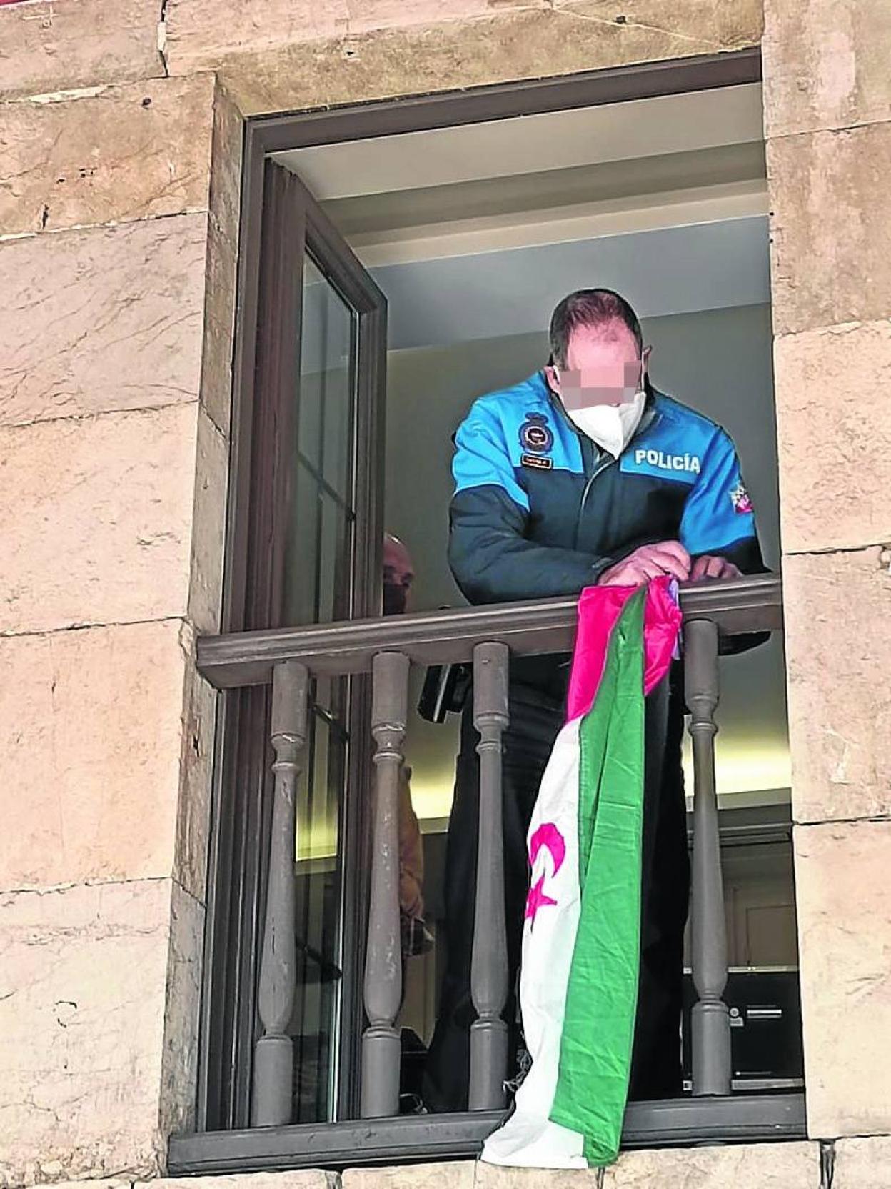 Un policía procede a retirar la bandera colocada por Cambia Avilés. 