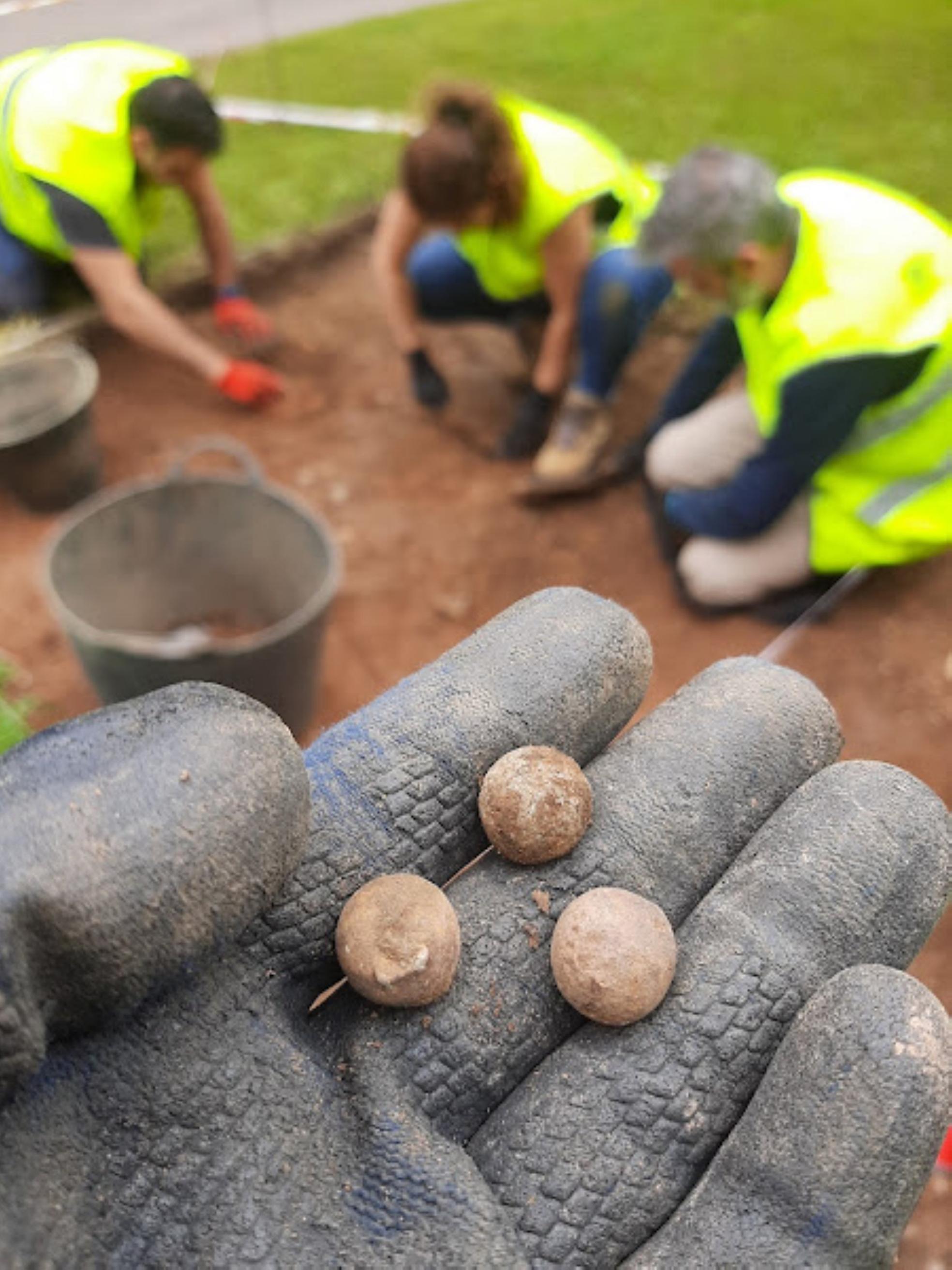 Excavación. Muestra de tres balas, al fono el equipo de arqueólogos trabajando. 