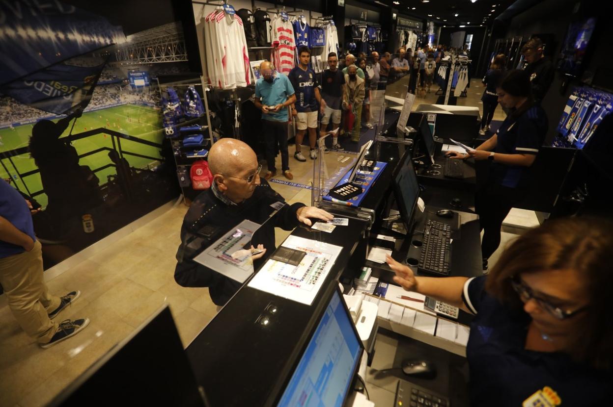 Un veterano abonado retira su carné con una cola de aficionados dentro de la tienda del Ovieo. 