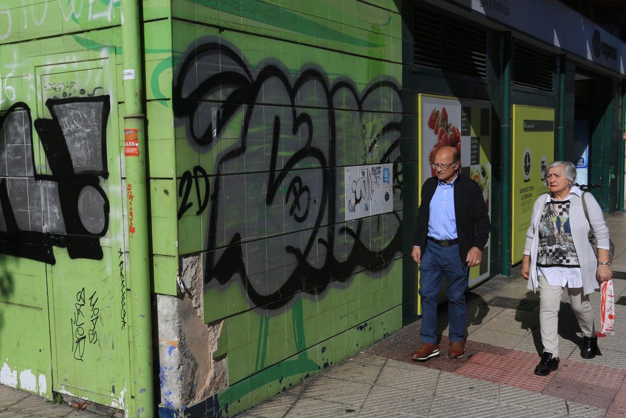 Dos personas pasan por delante de una fachada cubierta de pintadas. 