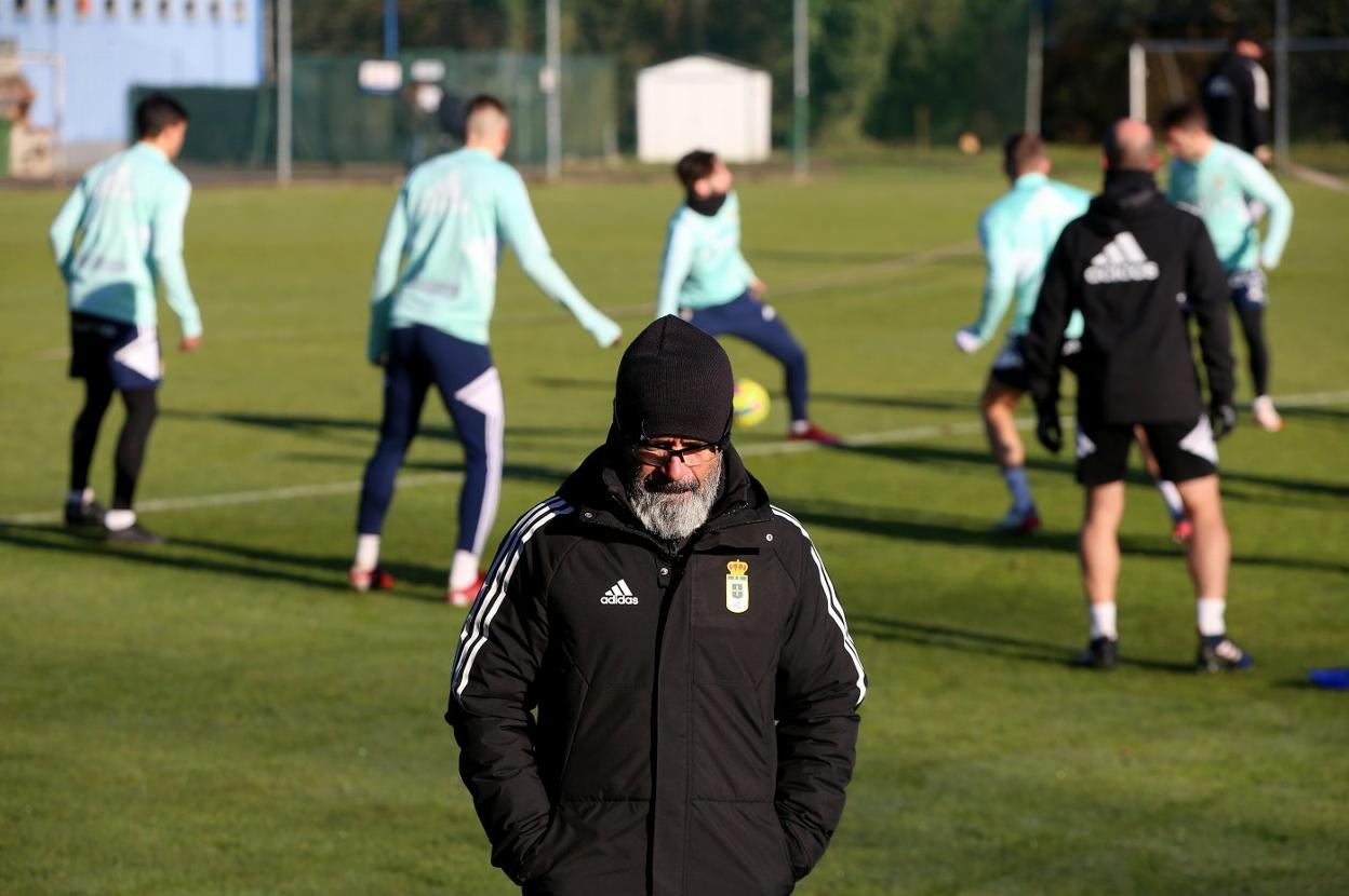 Álvaro Cervero, en primer plano, pensativo, mientras un grupo de jugadores realiza un rondo en El Requexón. 