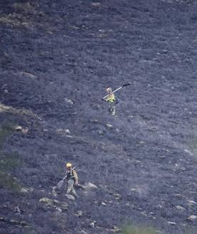 Imagen secundaria 2 - A la izquierda, un bombero lucha contra las llamas en el incendio de Blimea, que llegó a amenazar a zonas habitadas. En la derecha, dos bomberos peinan una zona devastada por las llamas. 