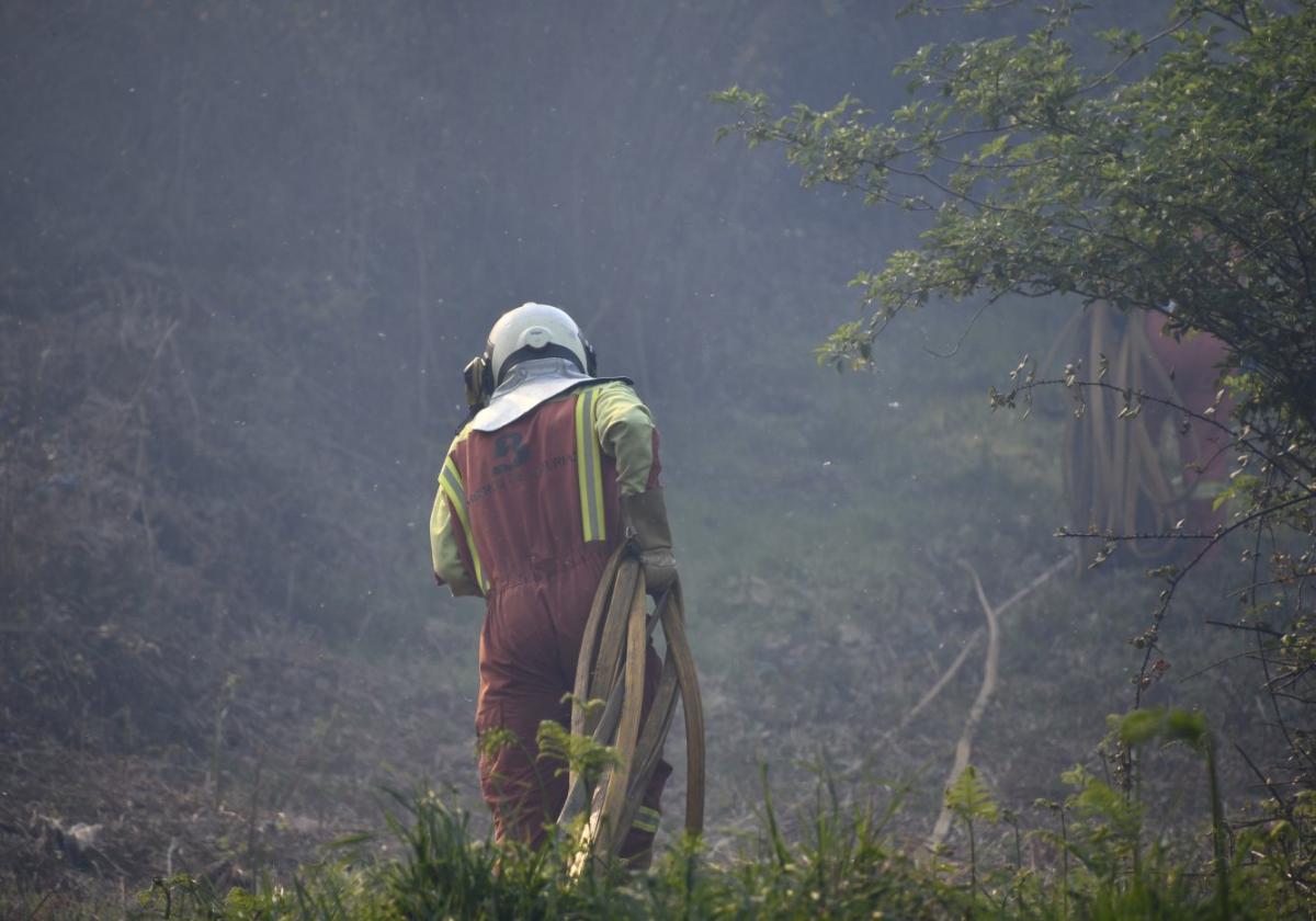 Un bombero carga con la manguera para frenar el fuego en Castrillón.