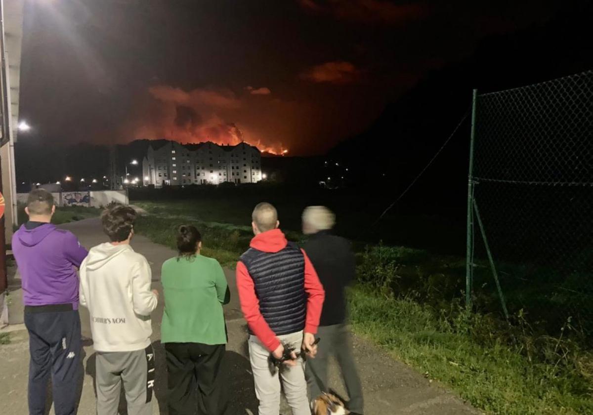 Varios vecinos de Valdés, que pasaron la noche en el polideportivo de Luarca, miran las llamas, que llegaron a las proximidades de la villa.