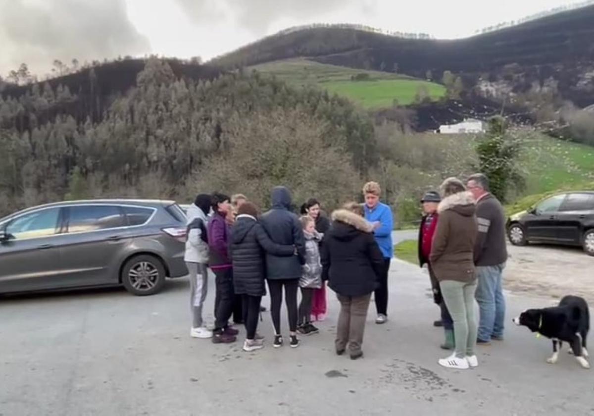 Vecinos de Enverniego reunidos en torno a María del Carmen. Al fondo, la devastación que dejaron los incendios.