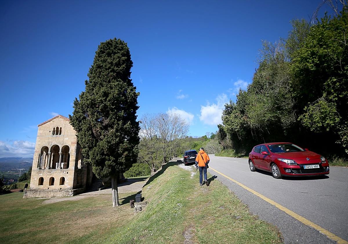 Un hombre pasea por el camino de tierra junto a la carretera mientras pasa un coche.