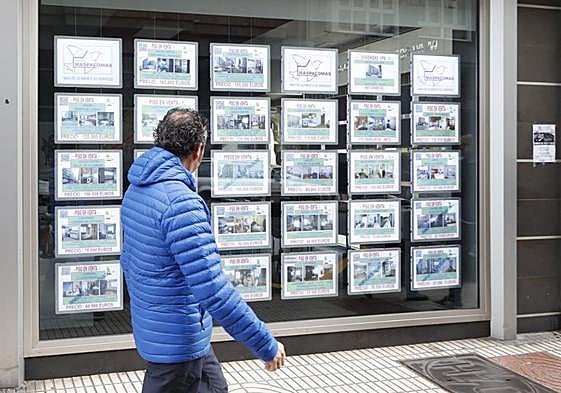 Un hombre camina junto a una inmobiliaria en la que se muestran las viviendas en venta.