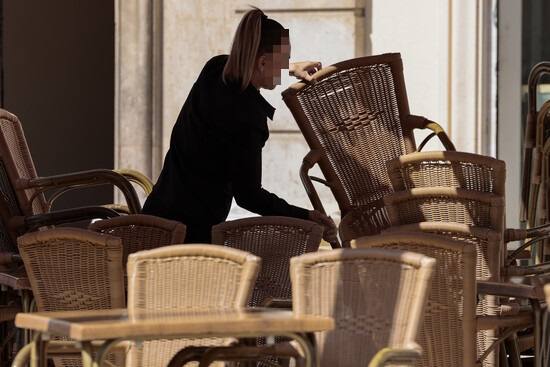 Una camarera colocando una silla en una terraza.