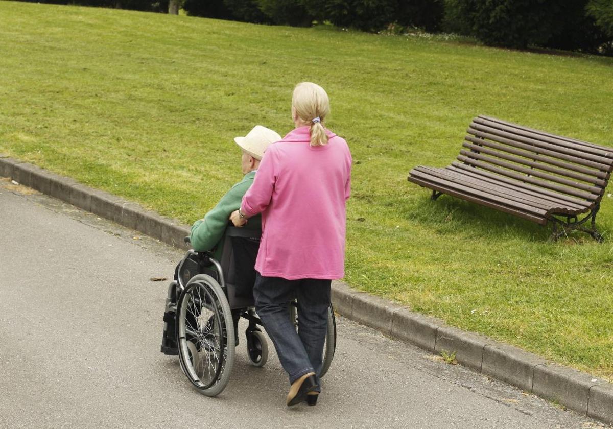 Una mujer ayuda a pasear a un usuario de silla de ruedas.