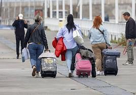Unas turistas caminan con sus maletas por el Muelle de Gijón.