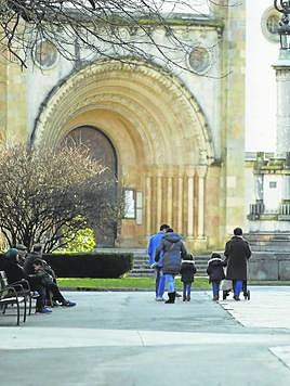 Una familia pasea por el Parque Viejo de La Felguera, con varias personas mayores sentadas en un banco.
