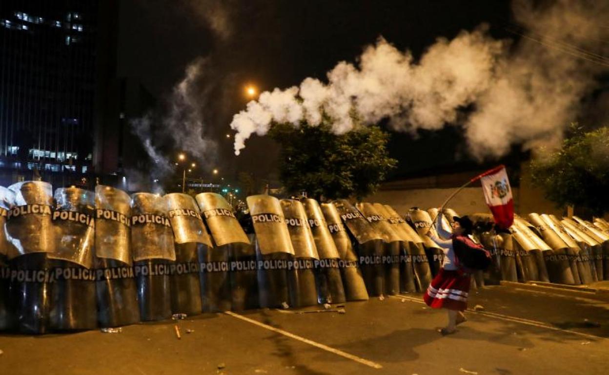 Una mujer ondea una bandera peruana ante una formación defensiva de agentes de Policía durante una protesta en Lima.