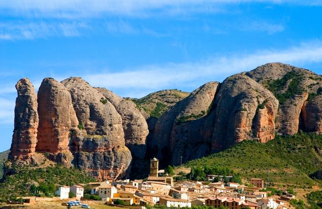 10. Agüero, Huesca. Conjunto Histórico. El lugar del Reino de los Mallos, grandes monolitos de piedra de color rojizo que son Monumento Natural, sobrevolados por buitres. Hay un sendero que los rodea. Tiene una famosísima iglesia románica de Santiago (siglo XII) con curiosas marcas de cantería que es Monumento Nacional. Está en plena España Vacía, a 46 km de Huesca, y la vista de los mallos al atardecer ya compensa el viaje.