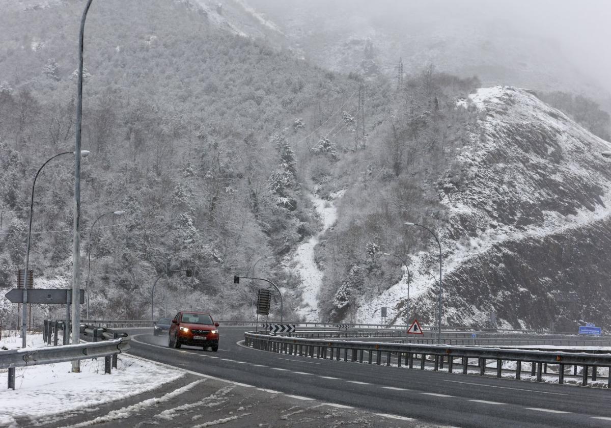 Dos turismos circulan por la autopista de peaje del Huerna, en medio de una nevada.