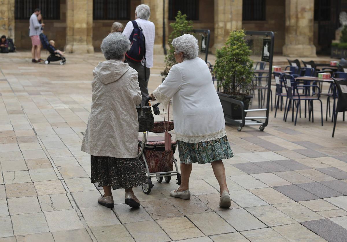 Dos mujeres pasean por la calle apoyadas en un andador para facilitar su caminata.