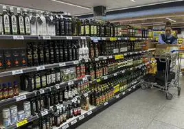 Una dependienta coloca aceites en un lineal del supermercado.