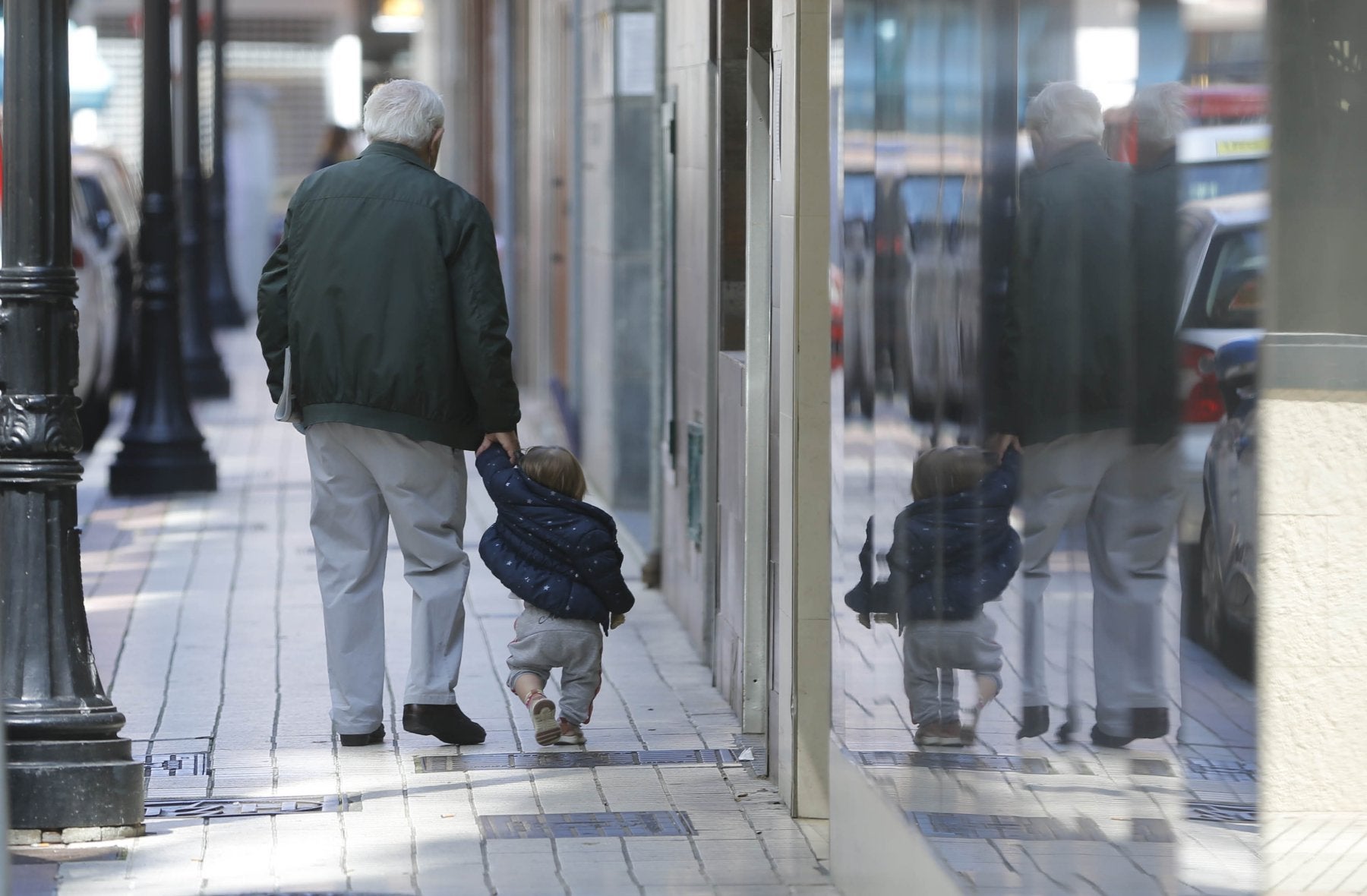 Un abuelo con su nieto caminan por una calle de Gijón.