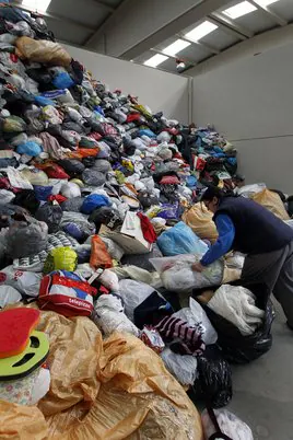 Montones de ropa usada preparada para su reutilización en una planta de reciclaje de Cáritas.