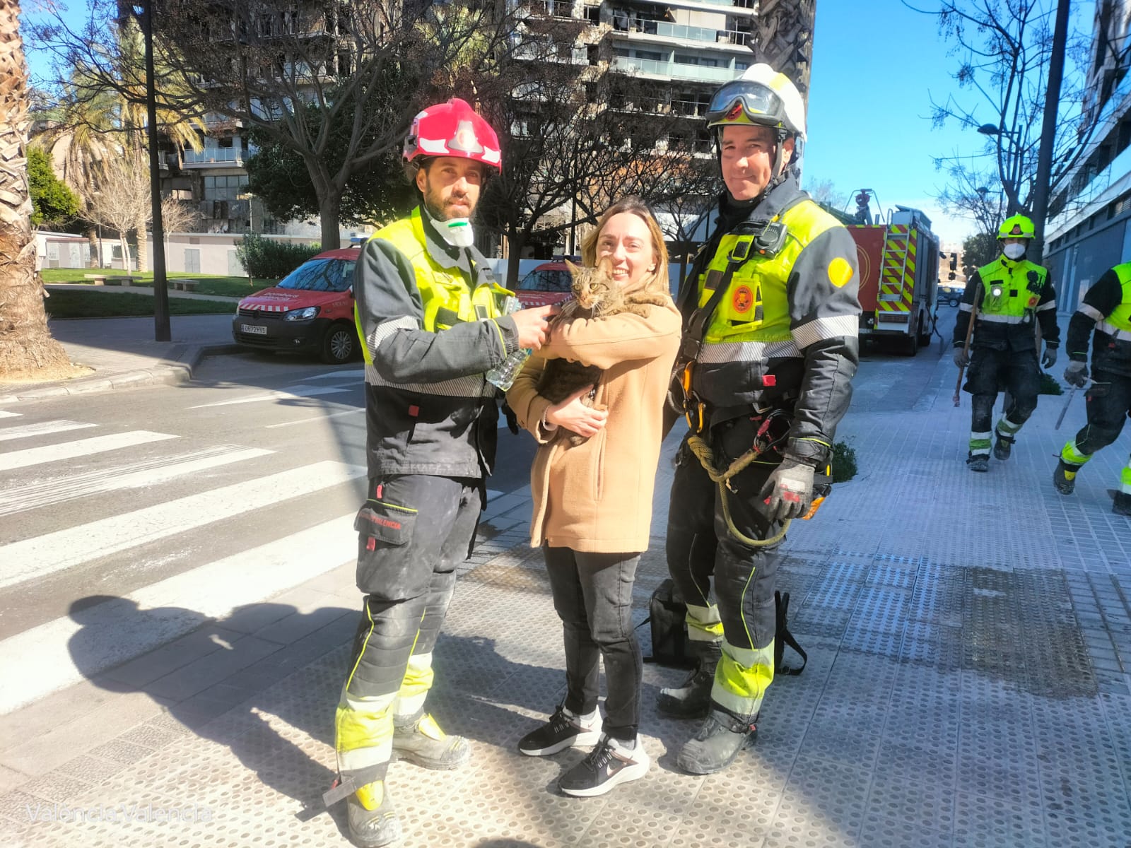 La dueña de 'Coco', con su gato y con los bomberos que rescataron al animal.
