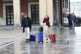 Una pareja de turistas caminan, con sus maletas, por la Plaza Mayor de Gijón.