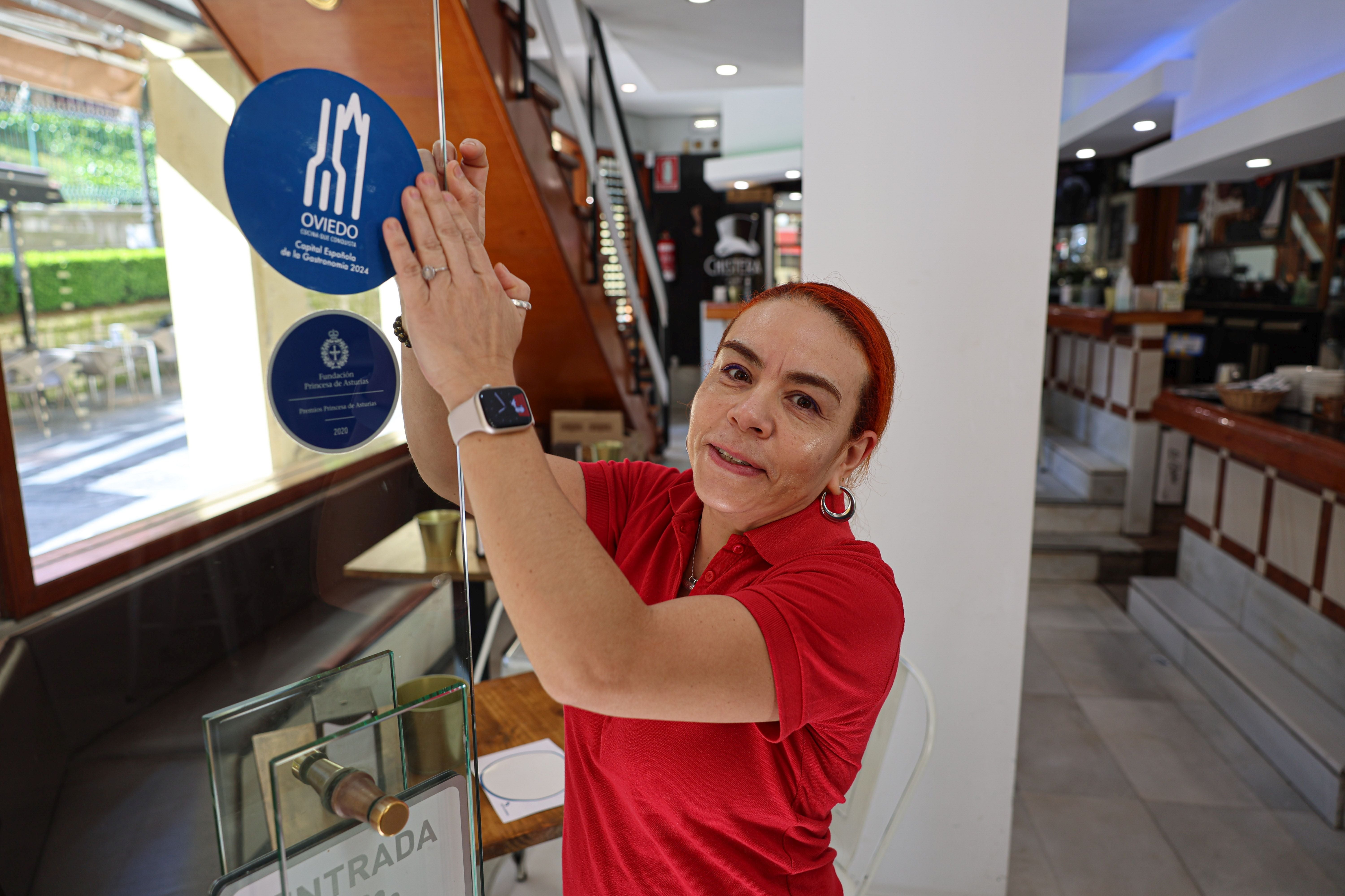 Una mujer coloca en un establecimiento hostelero la pegatina que anuncia Oviedo como capital gastronómica