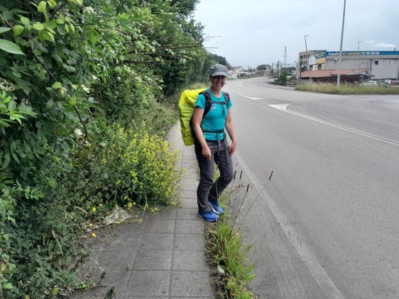 Una peregrina en la acera del Camino de Santiago, a la altura de Tamón, invadida por la vegetación.