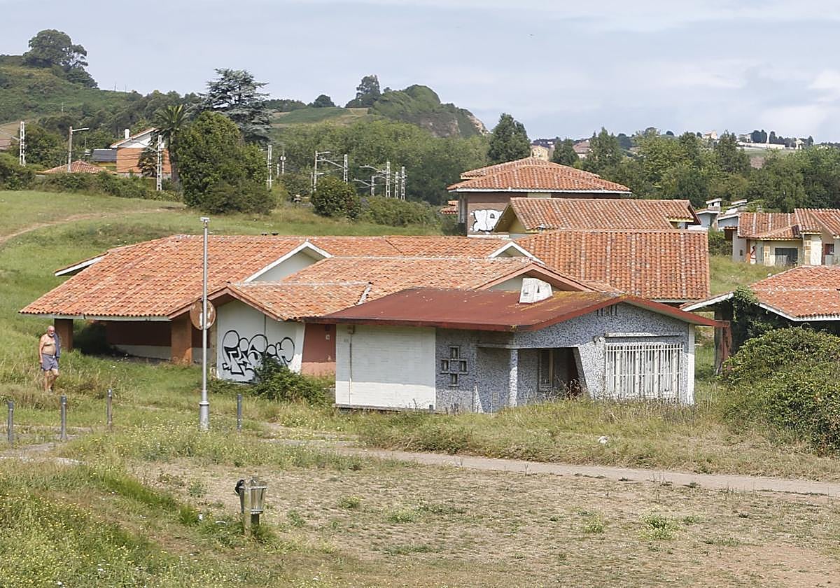 Dos personas toman el sol, en Perlora, con los edificios de la ciudad vacacional, en mal estado, al fondo.