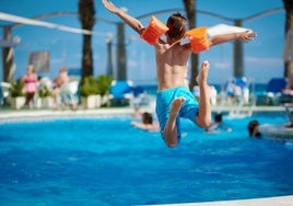 Un niño con un bañador azul se tira a una piscina.