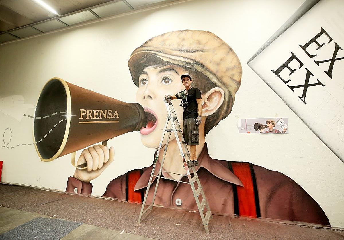 César Frey subido a la escalera delante del graffiti que dibuja en la Biblioteca de Asturias.