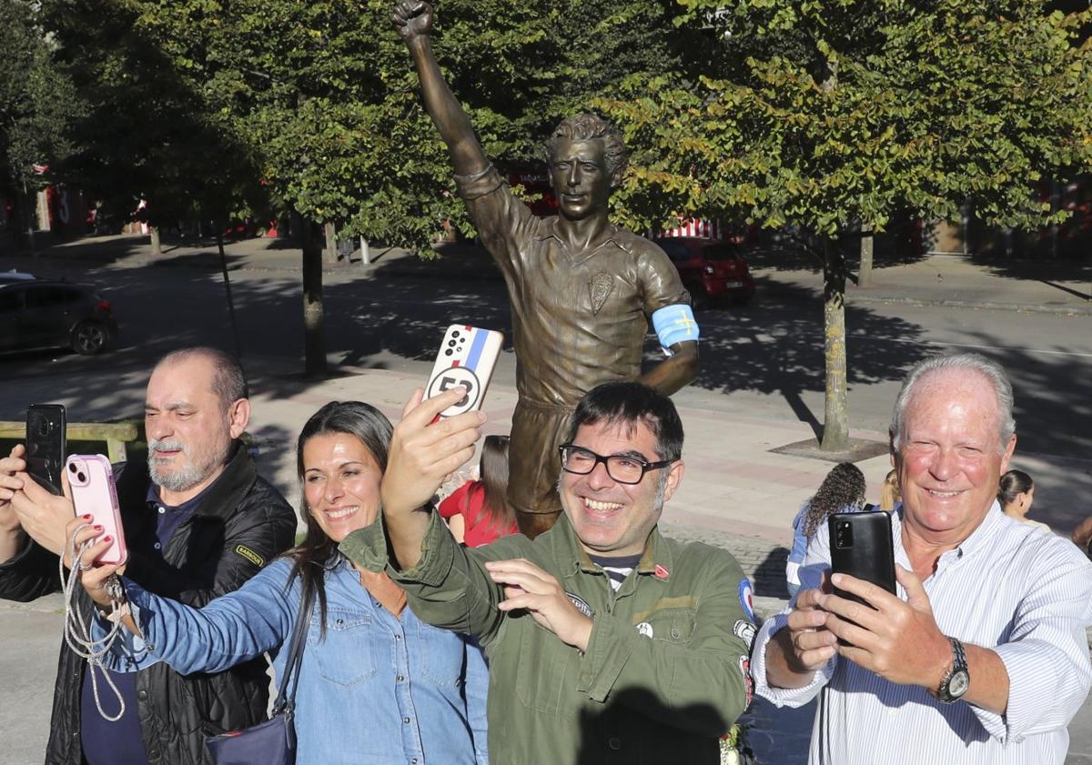 Imagen principal - Cuatro aficionados, ayer por la tarde, haciéndose un selfi con la estatua de Quini. Foto de grupo de unos seguidores con 'El Brujo'. Un aficionado, ayer, haciendo una foto a la estatua.