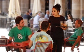 Una camarera atiende a unos clientes en la terraza de un local de hostelería.