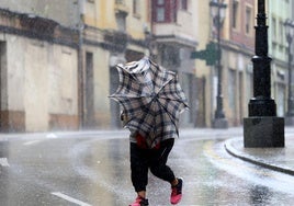 Una mujer intenta caminar en Oviedo, bajo la lluvia e intensas rachas de viento.