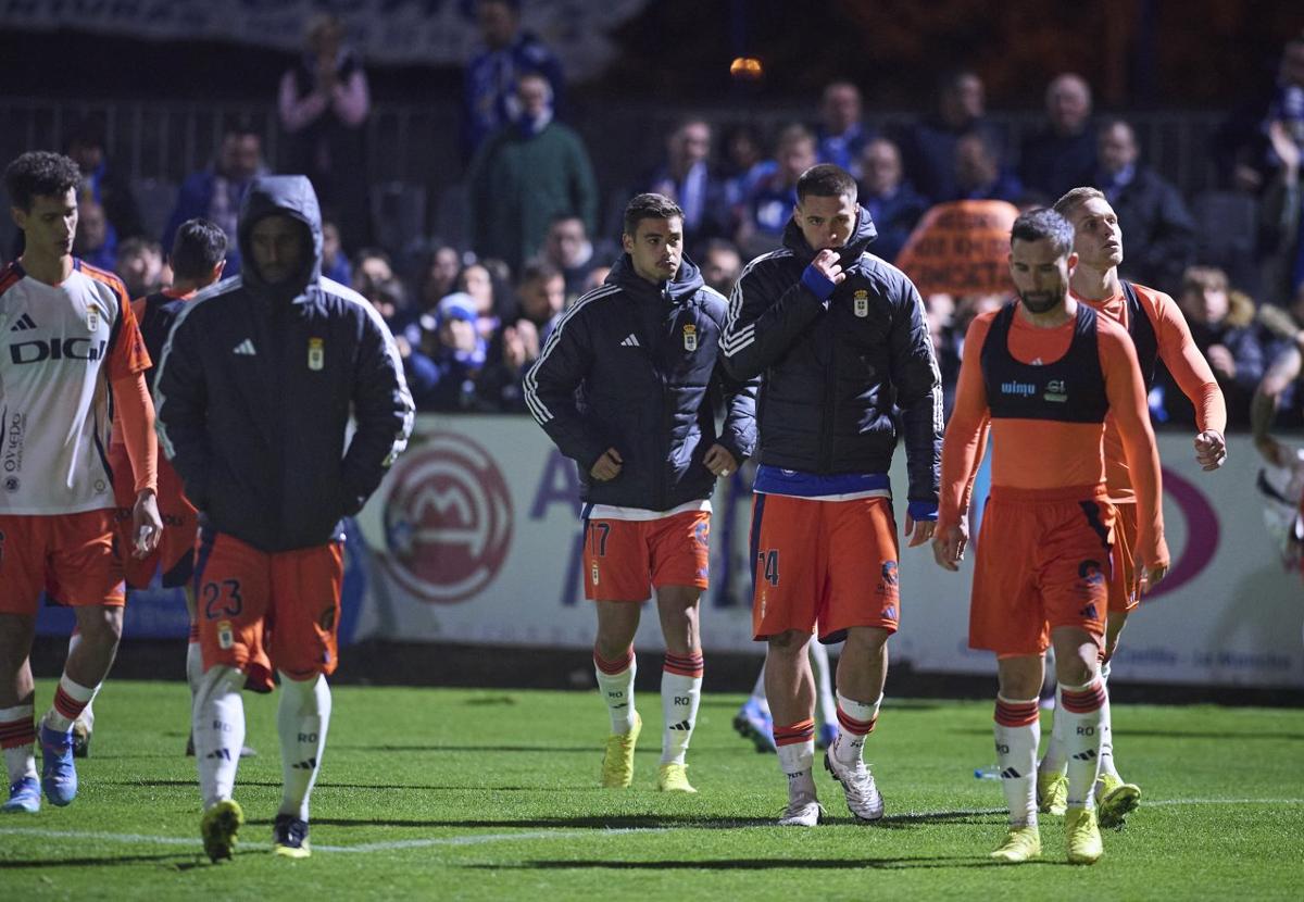 Los jugadores del Real Oviedo, cabizbajos al término del encuentro, con algunos de los aficionados azules presentes en el campo, al fondo.