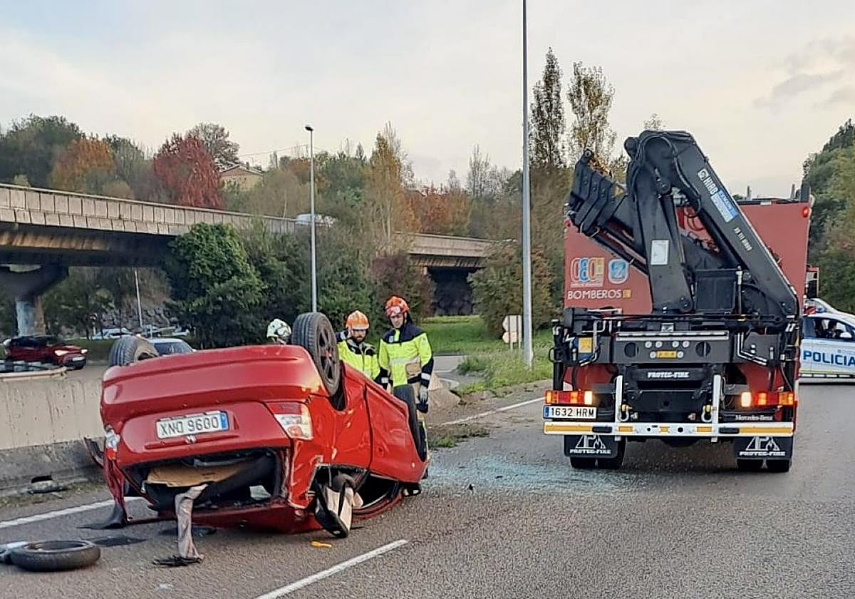Tres bomberos de Oviedo, frente al coche siniestrado, mientras una patrulla de la Policía Local asegura la vía, al fondo.