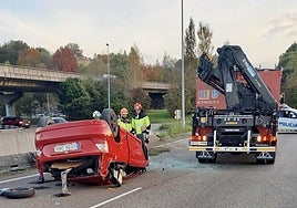 Tres bomberos de Oviedo, frente al coche siniestrado, mientras una patrulla de la Policía Local asegura la vía, al fondo.