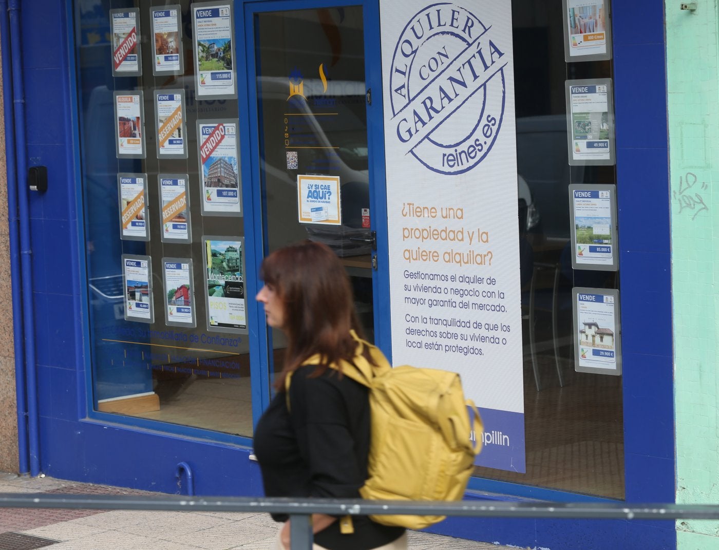 Una mujer camina por delante de una inmobiliaria.